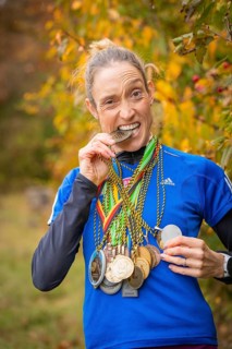Woman with medals playfully bites on a medal and smiles, middle distance runner Katharina Jaiser,