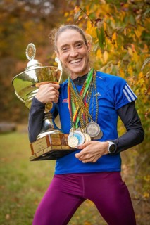 Happy woman holding trophy and medals in autumn surroundings, middle distance runner Katharina
