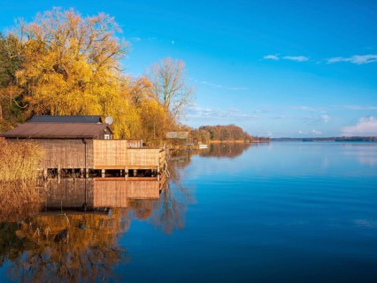 Shore with boathouses on Schaalsee in morning light, reeds and trees in autumn colors, Schaalsee