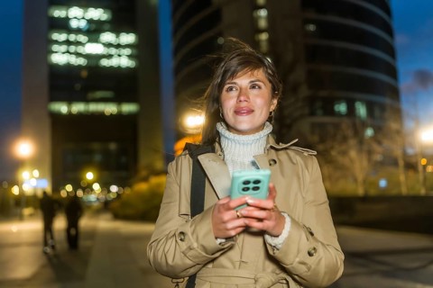 Woman standing outdoors at night, using a smartphone for communication and networking, dressed in a