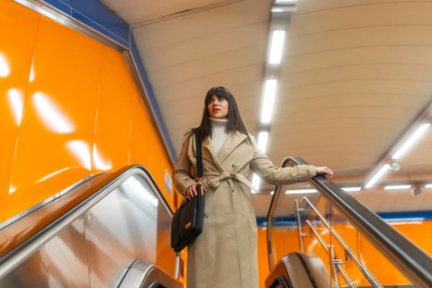 Woman travelling on an escalator in a subway station, holding onto the handrail, dressed in a