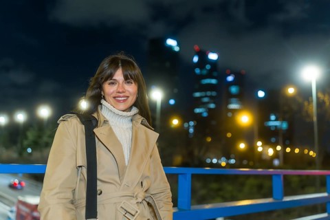 Young woman wearing a trench coat and turtleneck sweater smiling confidentially, standing outdoors