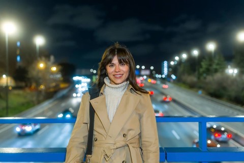 Woman smiling and standing on a bridge over a blurred highway with car lights creating bokeh,