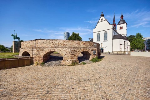 Historic railway hub, Alt St. Heribert church, equestrian statue, cobblestone walkway, lawn, trees,