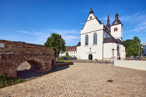 Historic railway hub, Alt St. Heribert church, cobblestone walkway, trees, pedestrians as