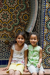 Two smiling girls in front of a wall with colorful tiles, alley in the old town, Souk, Fez El Bali,