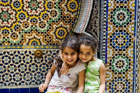 Two smiling girls in front of a wall with colorful tiles, alley in the old town, Souk, Fez El Bali,