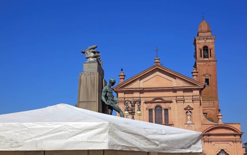 Monument with a statue in Piazza Unita and the Santo Stefano Collegiate Church in the city of