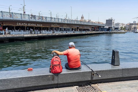 Istanbul, Turkey. June 23rd 2025. A mam sits fishing on the dockside in Eminonu beside the famous