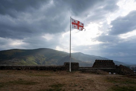 Dramatic heavy clouds and the Georgian flag over the mountain landscape surrounding Gori city