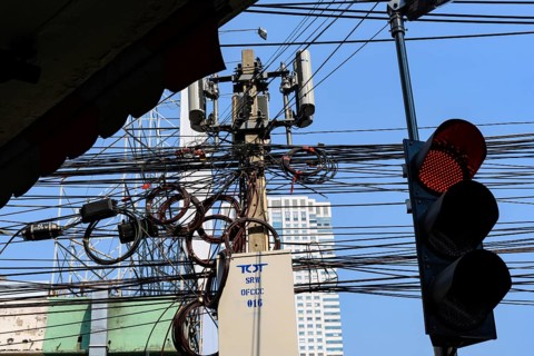 A red traffic light with a tangled mess of cables and wires with mobile communication mast, Bangkok