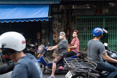 Bangkok, Thailand. March 18th 2025. An elderly couple wearing masks on a motor scooter in the busy