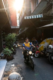 Bangkok, Thailand. March 18th 2025. A motorcycle mechanic rides through the narrow streets of Talat
