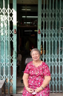 Bangkok, Thailand. March 18th 2025. A smiling older lady sitting outside a shop house in the