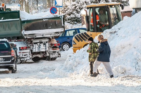 Two children playing among cars and loaders clearing snow on streets in Ystad, Skåne County,
