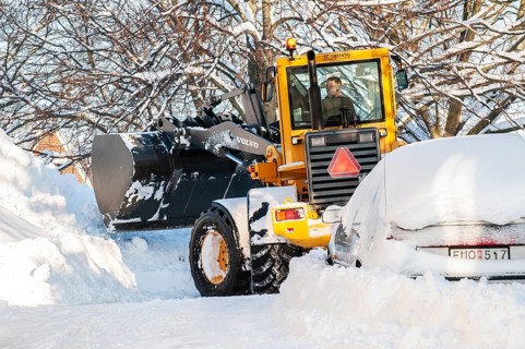 Loader clearing snow among snow-covered cars on streets in Ystad, Skåne County, Sweden, Scandinavia