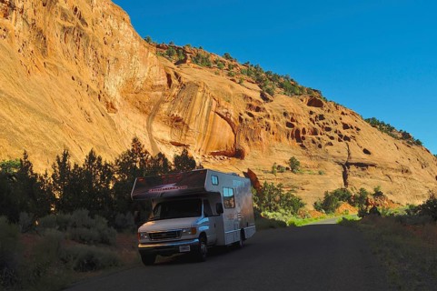 An RV parks on a road in a sunny rocky landscape with deep shade, Grand Staircase Escalante