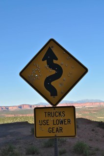 A road sign with serpentines strewn with bullet holes in a bare landscape with rolling hills in the