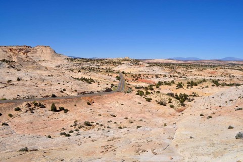 Paved road winds through dry landscape with reddish hills and sparse vegetation, Grand Staircase