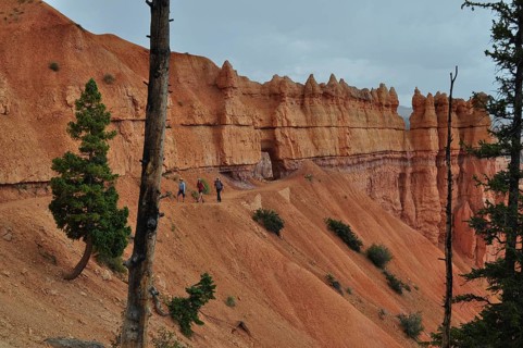 Hikers on a trail along dramatic red cliffs under looming clouds, Bryce Canyon National Park, Utah,