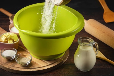 Flour falls into a green bowl surrounded by baking ingredients