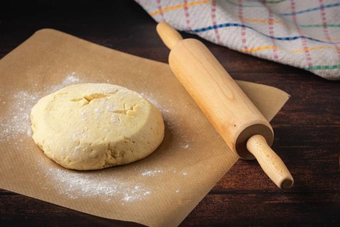 Dough on baking paper with a rolling pin next to it