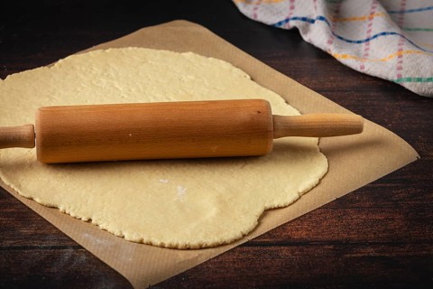 Dough is rolled out on baking paper with a rolling pin