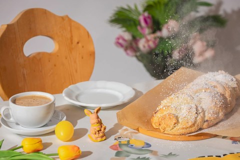 Yeast braid is sprinkled with sugar, breakfast table with coffee and decoration for Easter