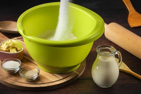 Sugar falls into a green bowl surrounded by baking ingredients