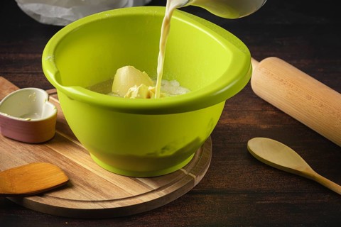 Milk is poured into a green bowl with other baking ingredients