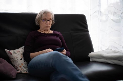 Elderly woman with glasses, gray hair, sitting on sofa and using smartphone, cell phone, Stuttgart,