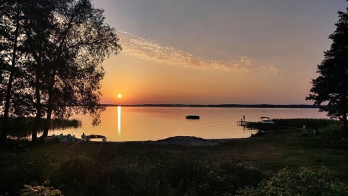A quiet, atmospheric sunset on a lake with trees and a boat dock, bicycle tour through Masuria,
