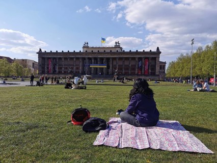 A woman sits on the meadow in front of the old museum on Museum Island in Berlin with the Ukrainian