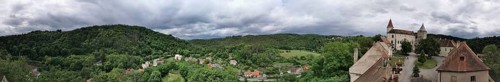 Panoramic view of a hilly landscape with a castle complex and thick greenery under cloudy sky,
