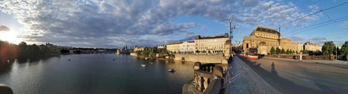 Extensive city panorama of Prague with the Vltava River, a bridge with tram and historic buildings