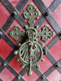 Decorative door knocker on red background decorated with coat of arms and metal ornaments, Poland