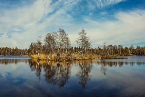 Calm lake with trees and clouds reflecting in the water. Autumn atmosphere with blue sky,