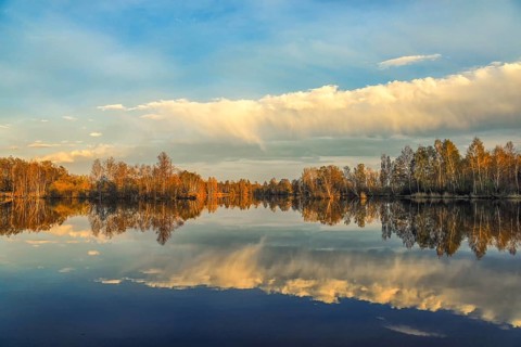Tranquil landscape with autumn trees reflecting in the still lake, surrounded by a blue sky with