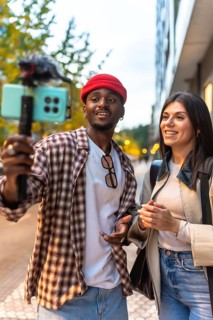 Diverse couple vlogging outdoor, enthusiastically recording video on a smartphone with a microphone