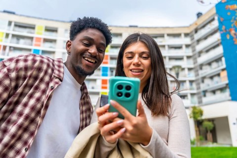 Young diverse friends smiling and sharing content on a smartphone outdoors, enjoying social media,