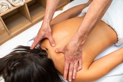 Professional masseur intensely massaging the back of a female client lying on a treatment table,