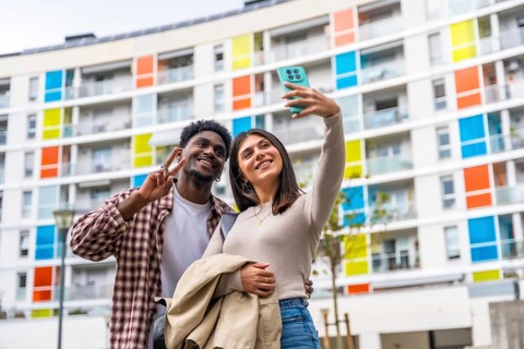 Happy diverse couple smiling and posing for a smartphone selfie, showing a peace sign while