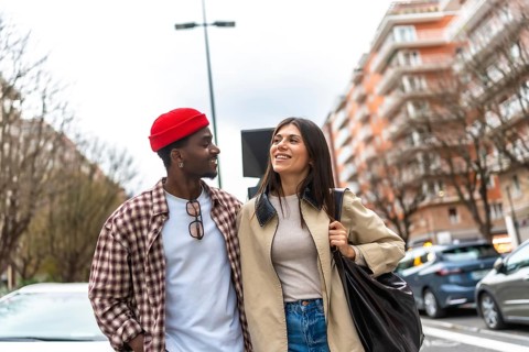 Interracial couple smiling and walking down a vibrant city street, sharing a candid moment of joy,