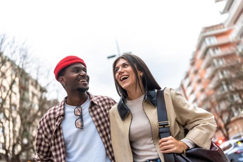 Young diverse couple walking and laughing on a city street, sharing a joyful, candid moment of