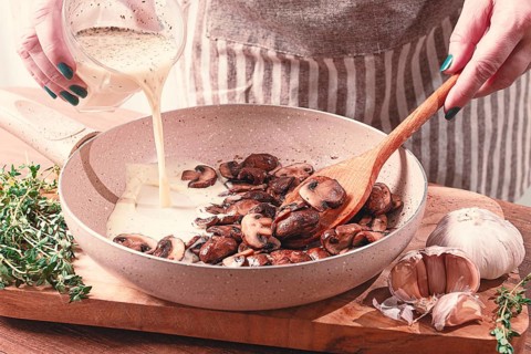 Cooking sauce with mushrooms, a woman pours cream into a pan with mushrooms, natural light,