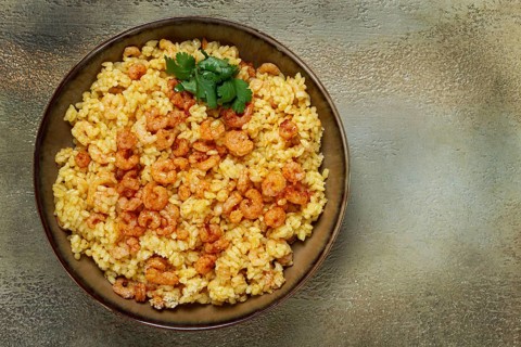 Risotto with shrimp, in a bowl, on a textured surface, with a side dish of fresh coriander,