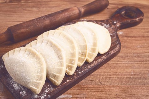 Raw chebureks, mini, on a cutting board, wooden table, close-up, no people