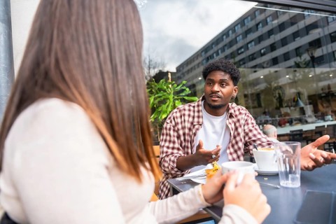 Young man and woman sit at an outdoor cafe in the city, sharing coffee and a serious conversation