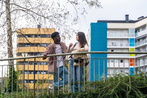 Two young adults, african american man and caucasian woman, chatting and leaning on a metal railing