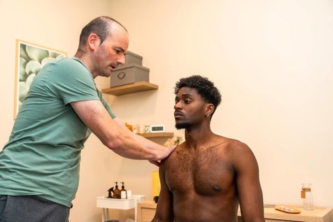 Male practitioner examining a young man's shoulder, providing professional medical care during a